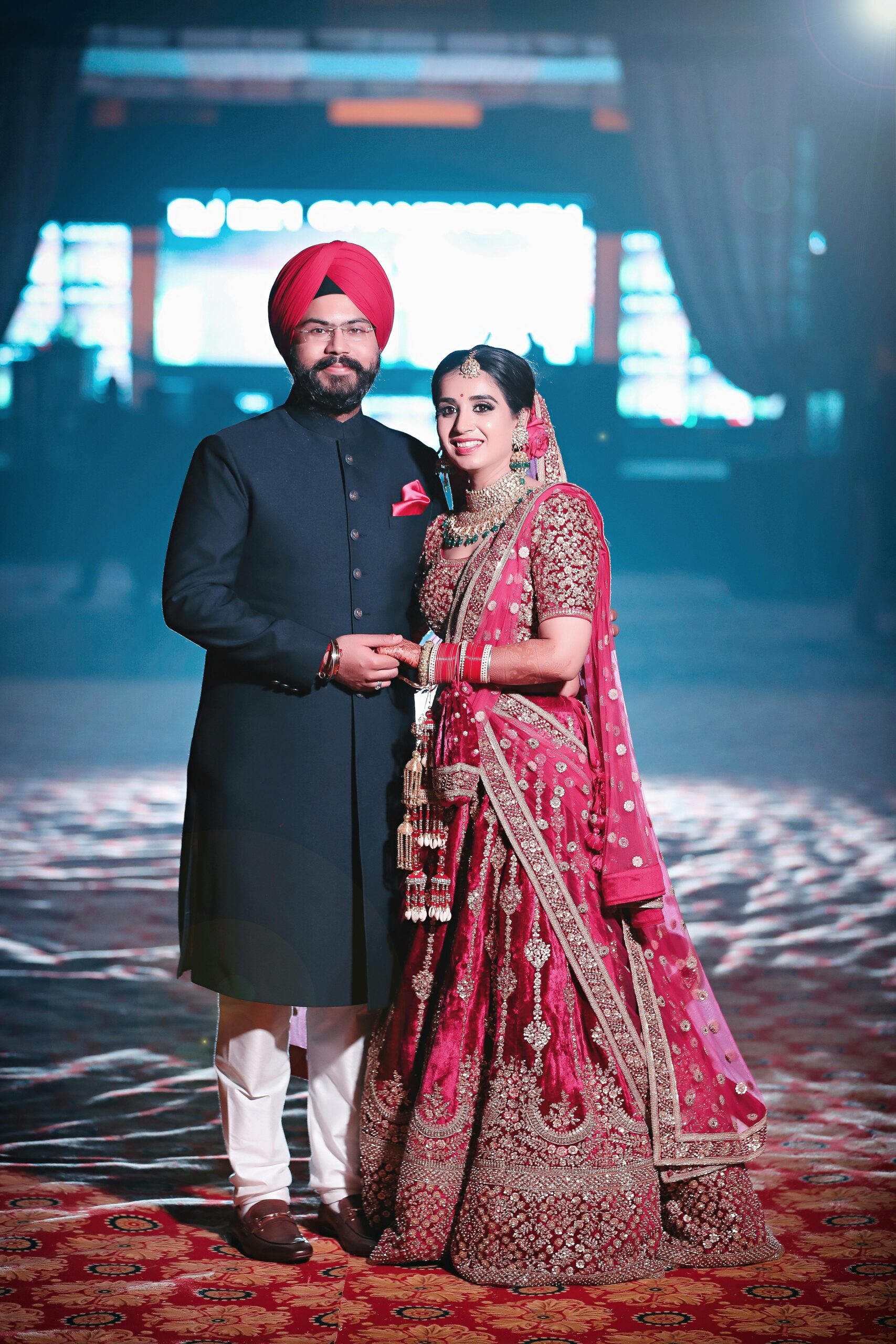 A joyful Indian couple in traditional wedding attire, celebrating their special day indoors.