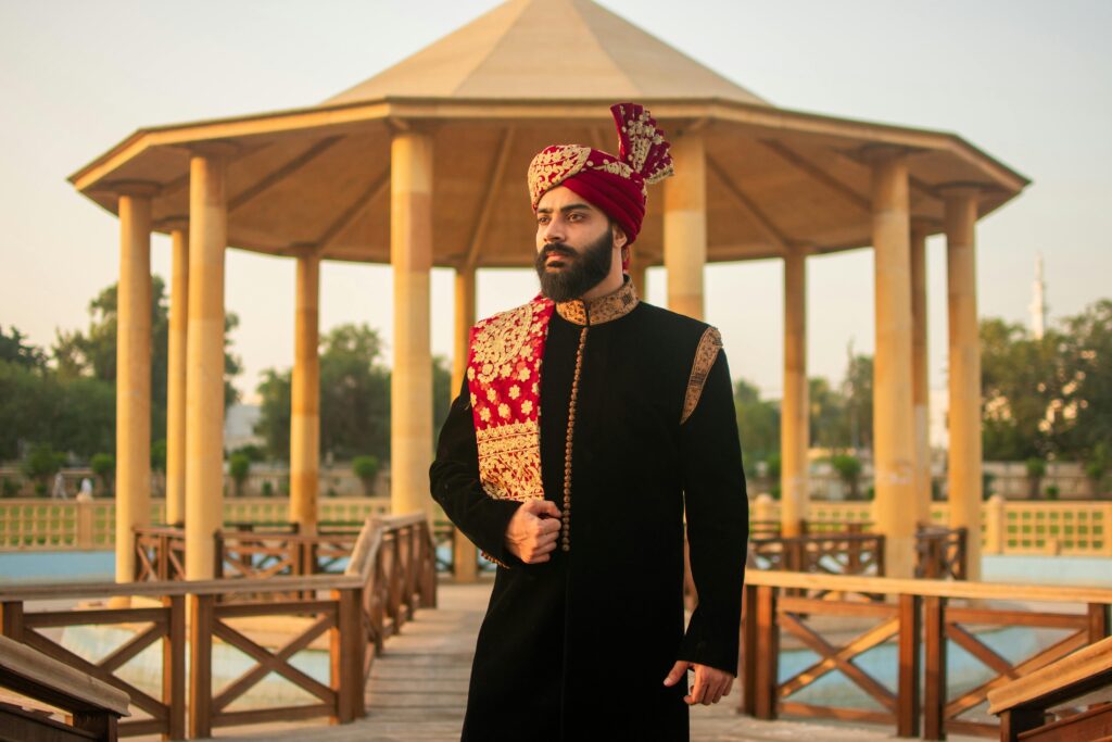 A man dressed in traditional Indian wedding attire standing outdoors under a pavilion.